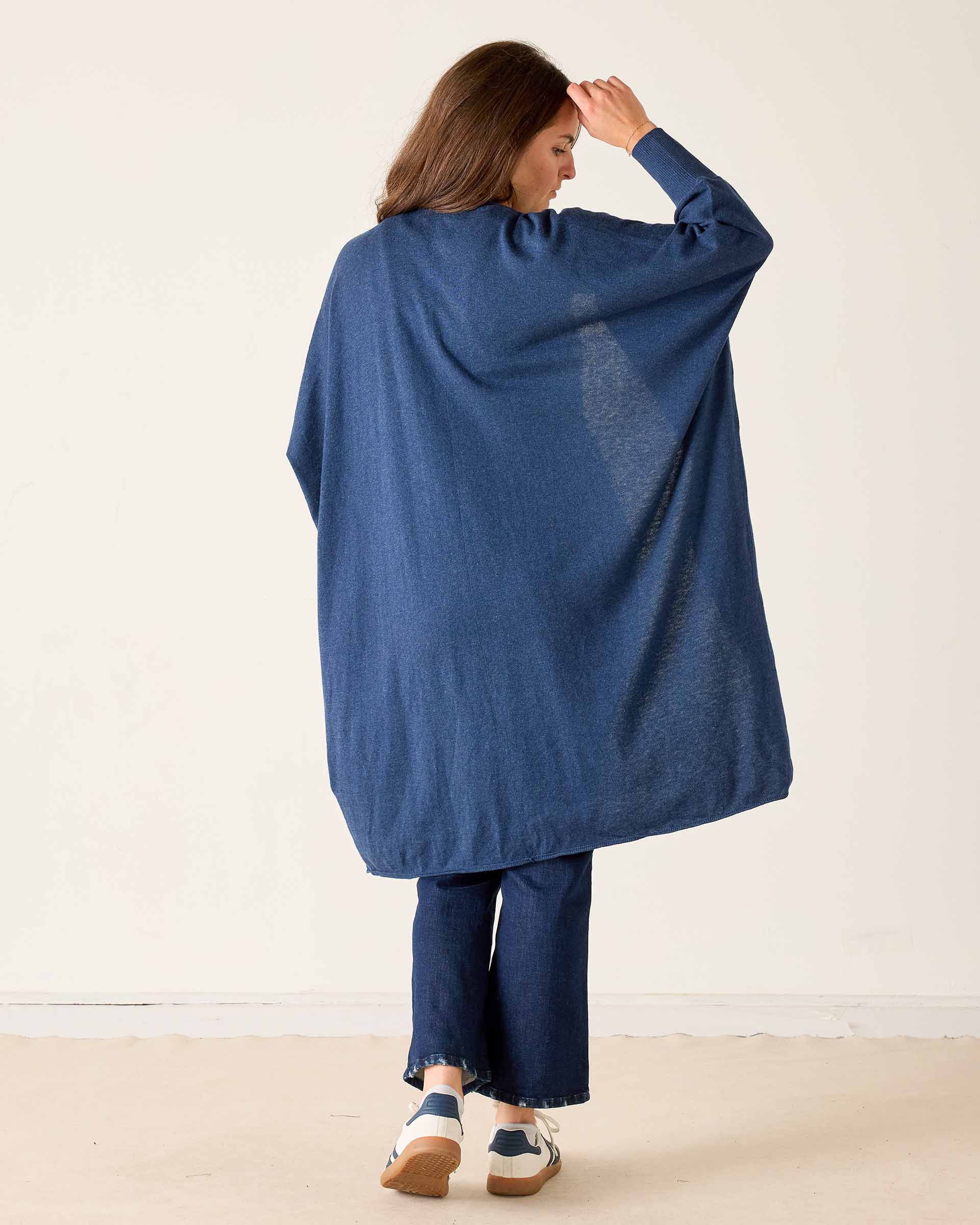 Woman wearing a blue poncho and pants against a white background