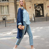 Woman walking on a city street wearing a blue cardigan, light blue shirt, and jeans.