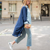 Woman walking on a street wearing a blue cardigan, light blue shirt, and jeans.