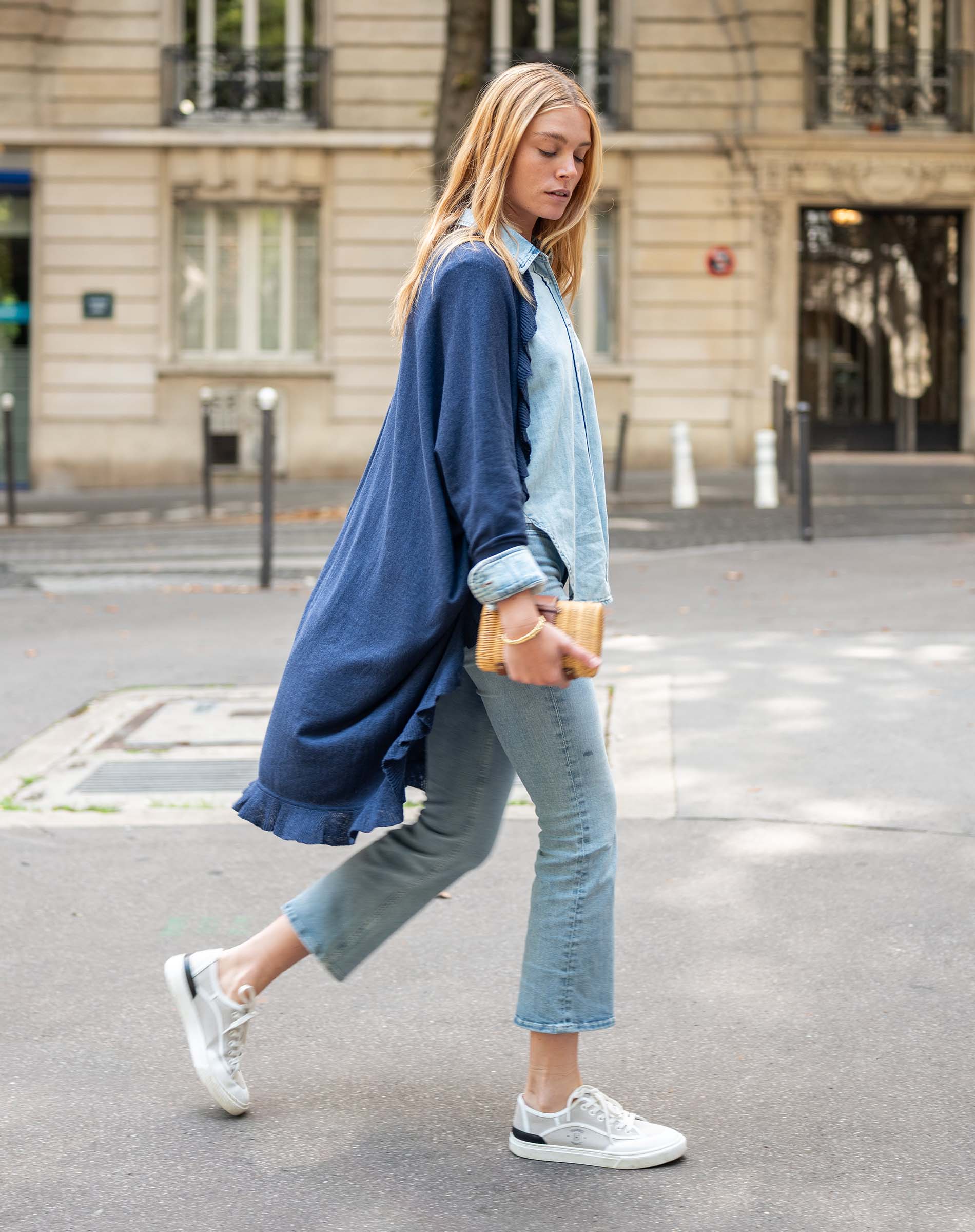 Woman walking on a street wearing a blue cardigan, light blue shirt, and jeans.