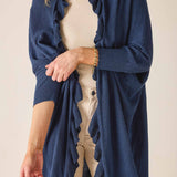 Person wearing a blue cardigan over a beige top and pants on a plain background