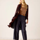 MERSEA women's travel-friendly women's travel-friendly chocolate ruffled kimono wrap worn over a brown knit top and high-waisted wide-leg jeans.