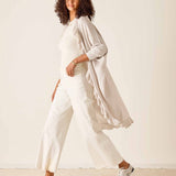 Woman wearing a white outfit with a light beige cardigan against a plain background