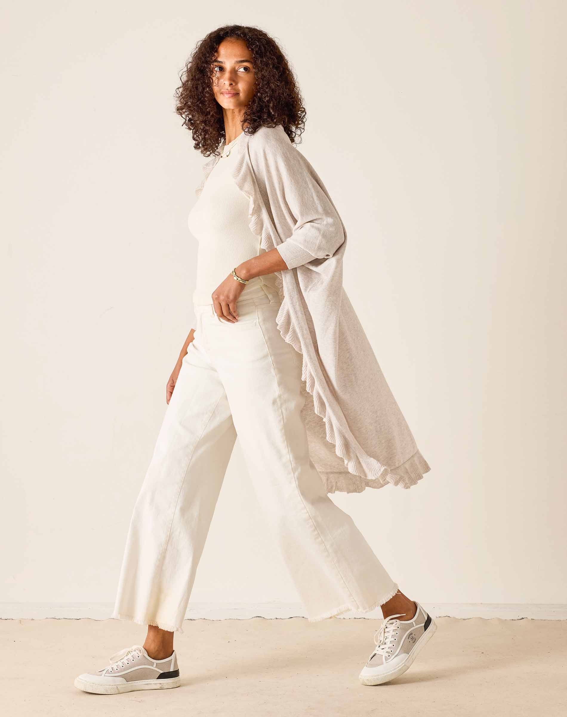 Woman wearing a white outfit with a light beige cardigan against a plain background