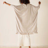 Person wearing a beige cardigan over a white outfit against a plain background