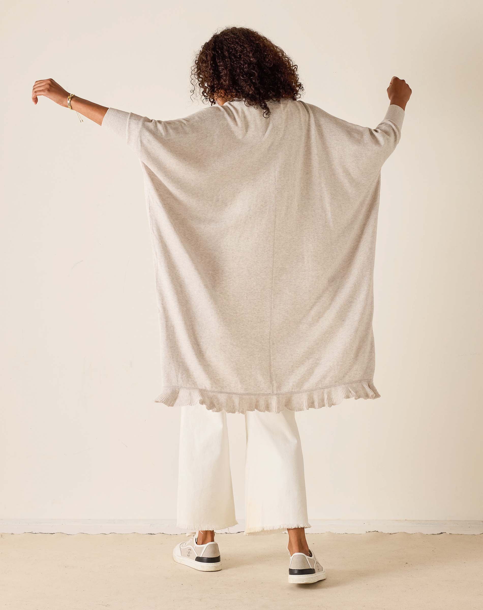 Person wearing a beige cardigan over a white outfit against a plain background
