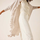 Woman wearing a light gray cardigan over a white top and pants on a plain background