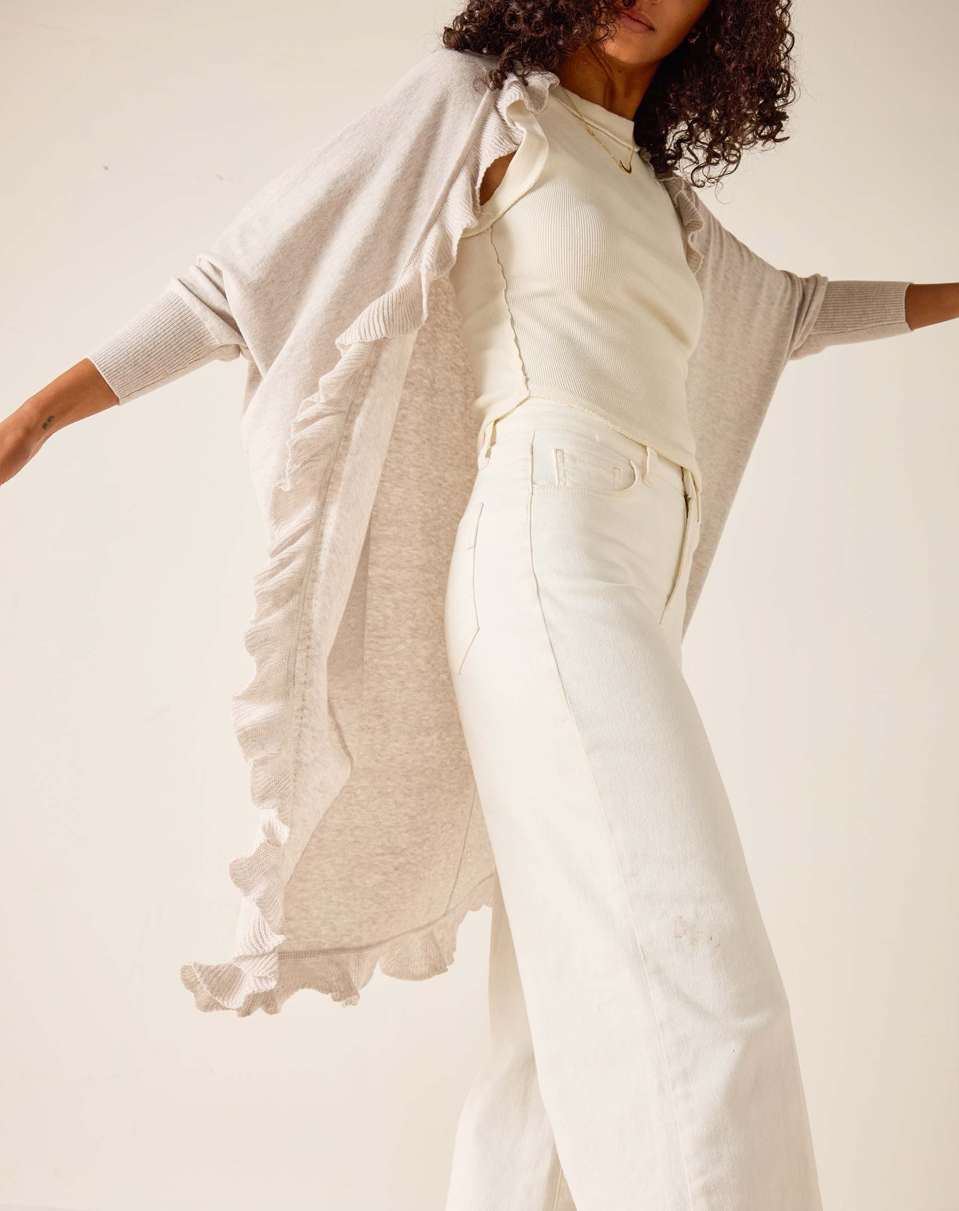 Woman wearing a light gray cardigan over a white top and pants on a plain background