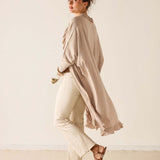 Woman wearing a beige long-sleeve top and white pants against a plain background