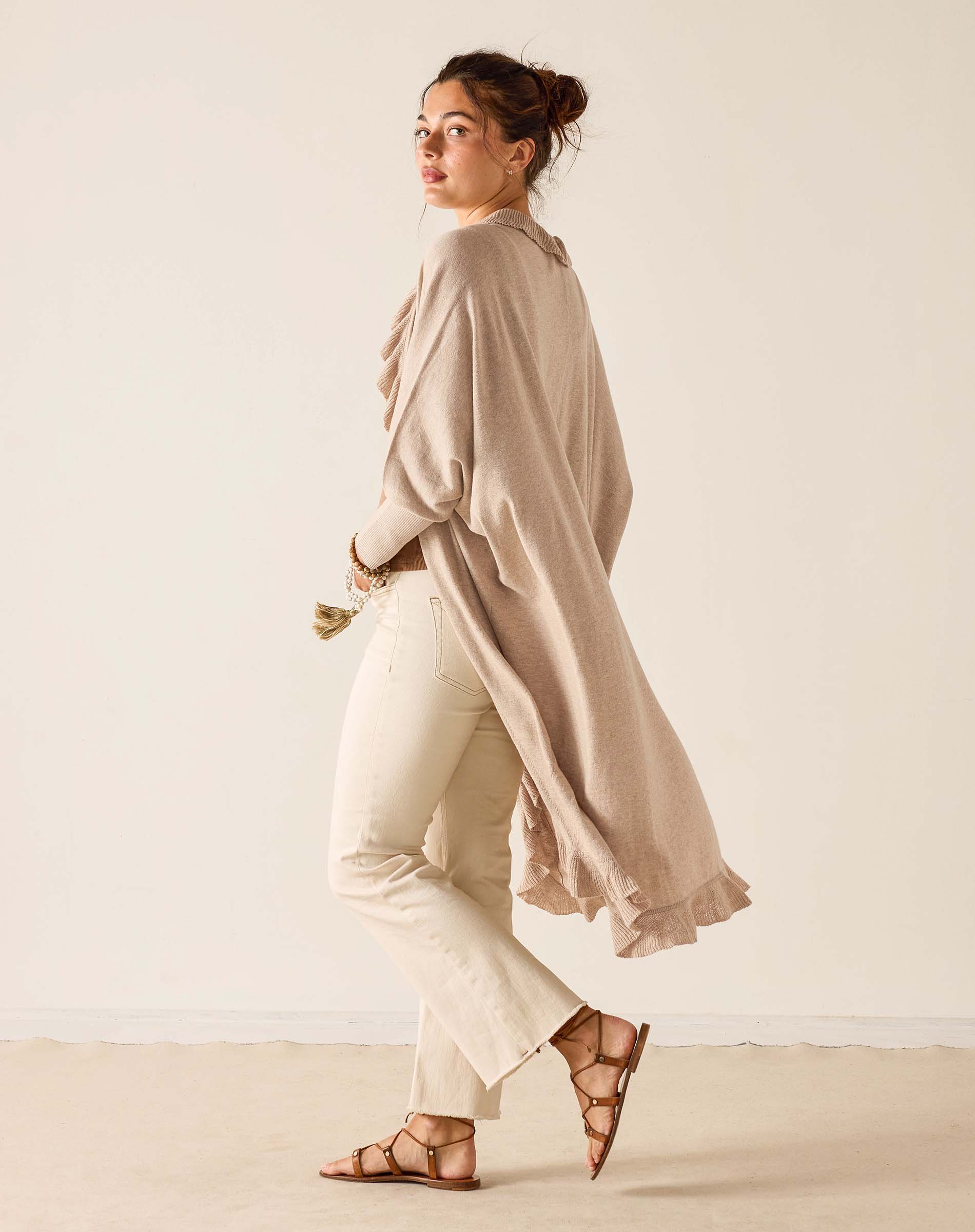 Woman wearing a beige long-sleeve top and white pants against a plain background