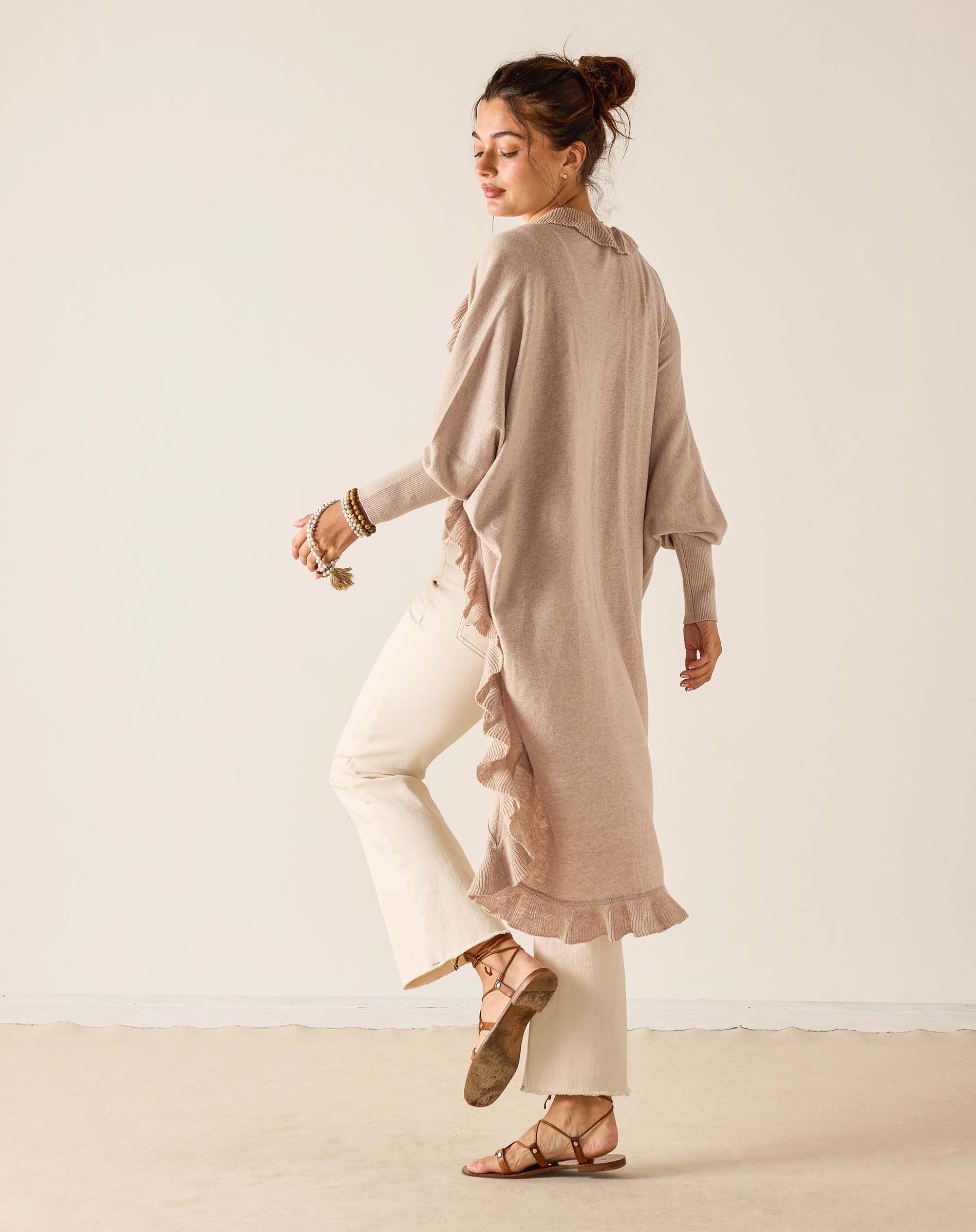 Woman wearing a beige long shirt and white pants against a plain background