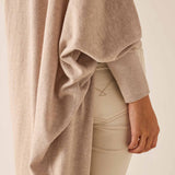 Beige sweater draped over a person wearing beige pants on a light background