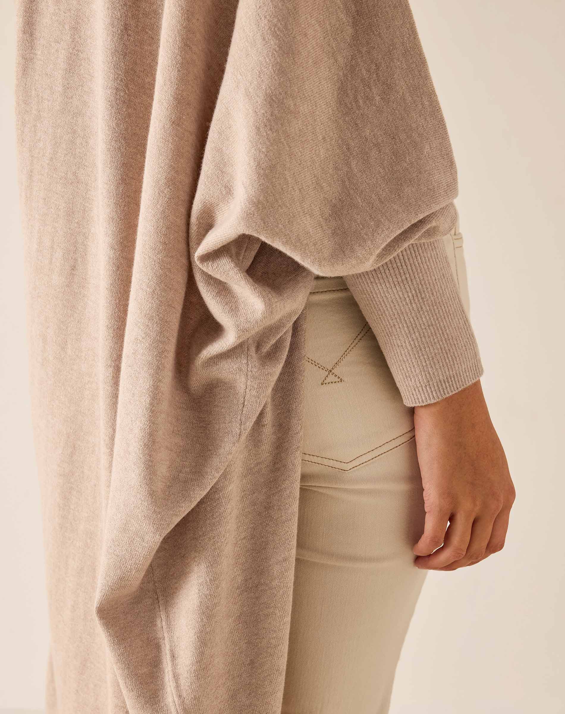 Beige sweater draped over a person wearing beige pants on a light background