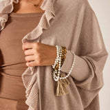 Person wearing a beige sweater with ruffled edges, holding a bracelet with tassels.