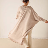Woman wearing a beige poncho and white pants against a plain background