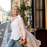 Woman walking on a street wearing a white shirt and light pink blouse with a yellow clutch.