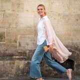 Woman walking against a stone wall wearing a white shirt, pink cardigan, blue jeans, and pink shoes.