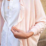 Person wearing a light pink cardigan over a white shirt with a neutral background