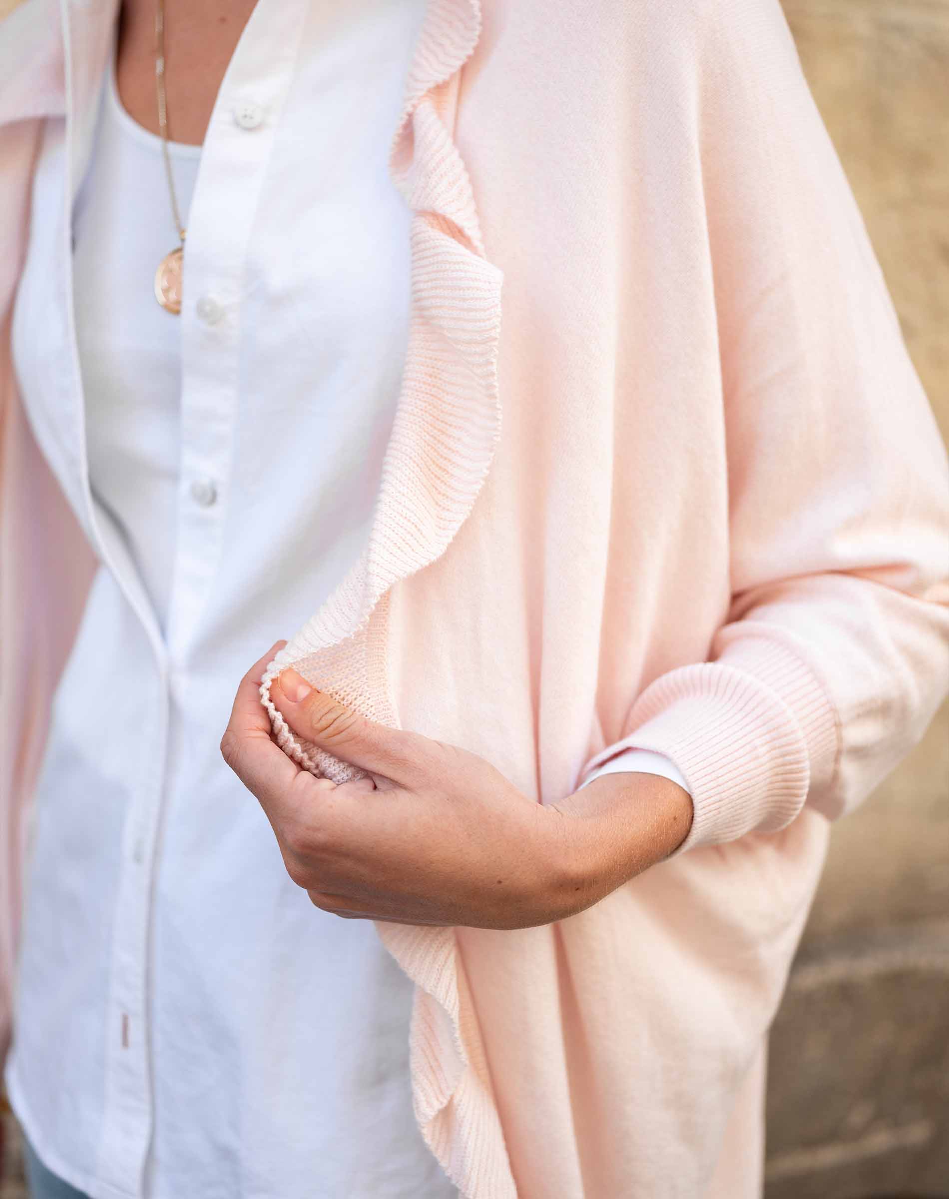 Person wearing a light pink cardigan over a white shirt with a neutral background