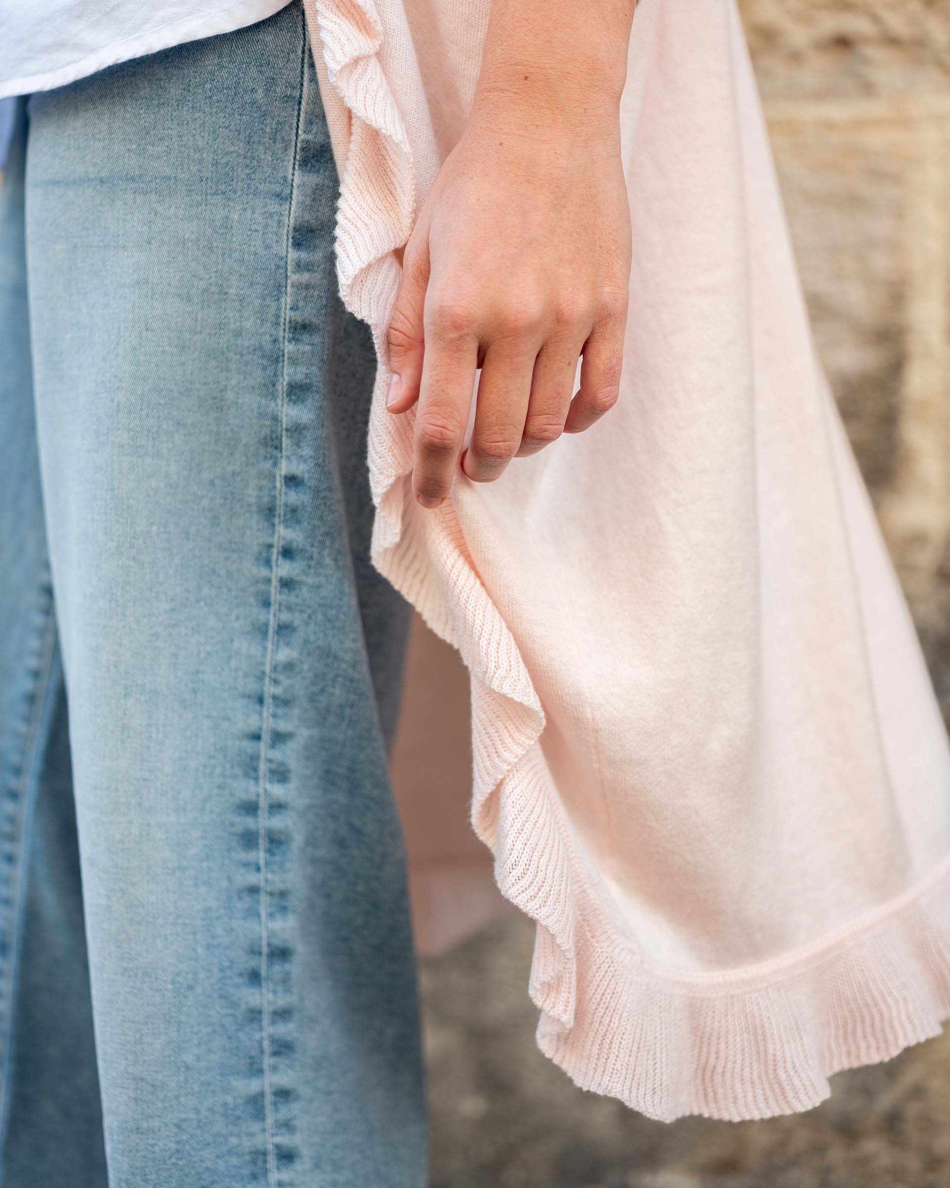Close-up of a person wearing light blue jeans and a pink blouse with ruffled details.