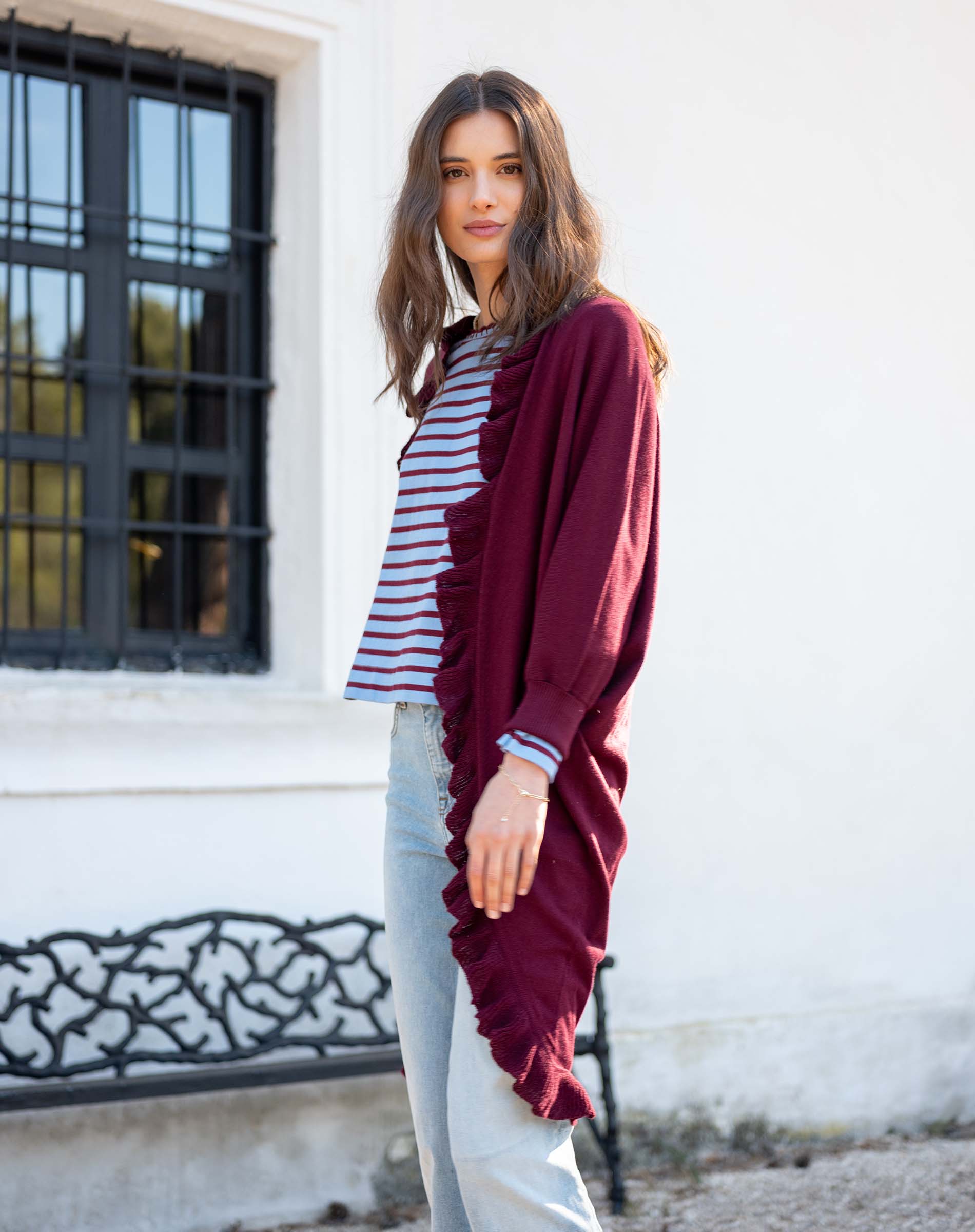 Model wearing a wine-colored ruffled kimono wrap over a striped tee and light-wash denim jeans.