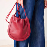 Red handbag held by a person wearing blue jeans on a plain background