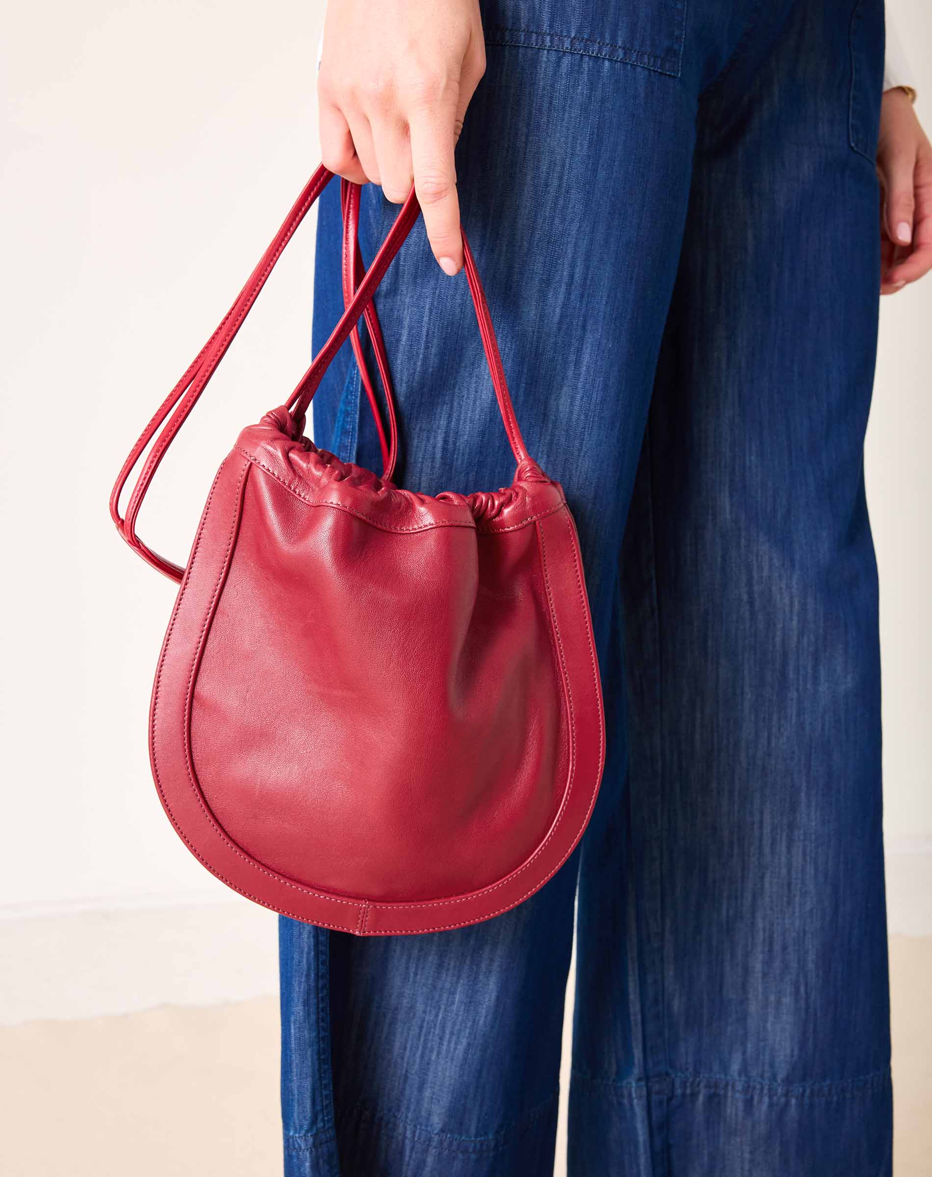Red handbag held by a person wearing blue jeans on a plain background