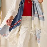 Person wearing a red top, white pants, and a striped shawl with fringes.