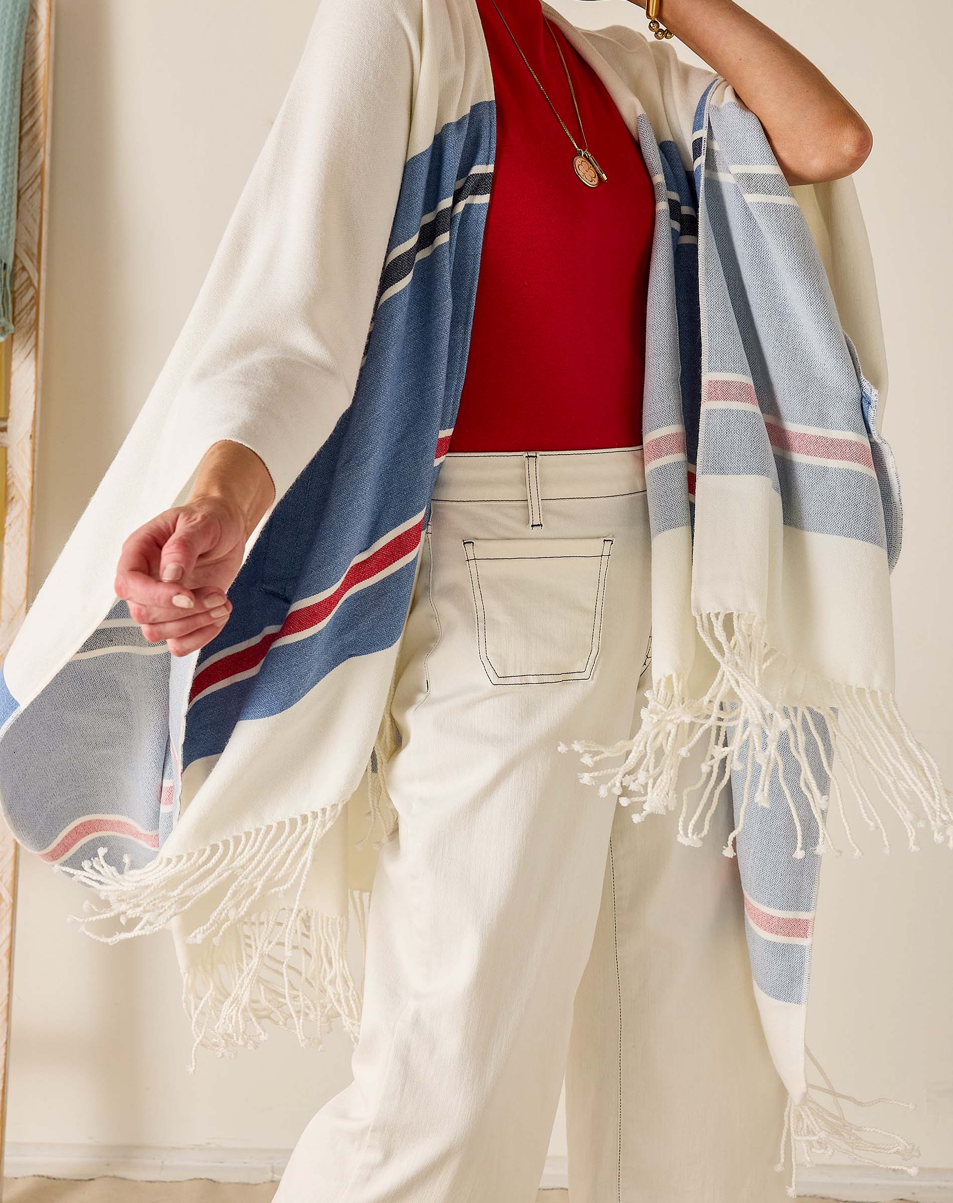Person wearing a red top, white pants, and a striped shawl with fringes.