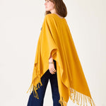 Woman wearing a yellow poncho with fringe on a white background