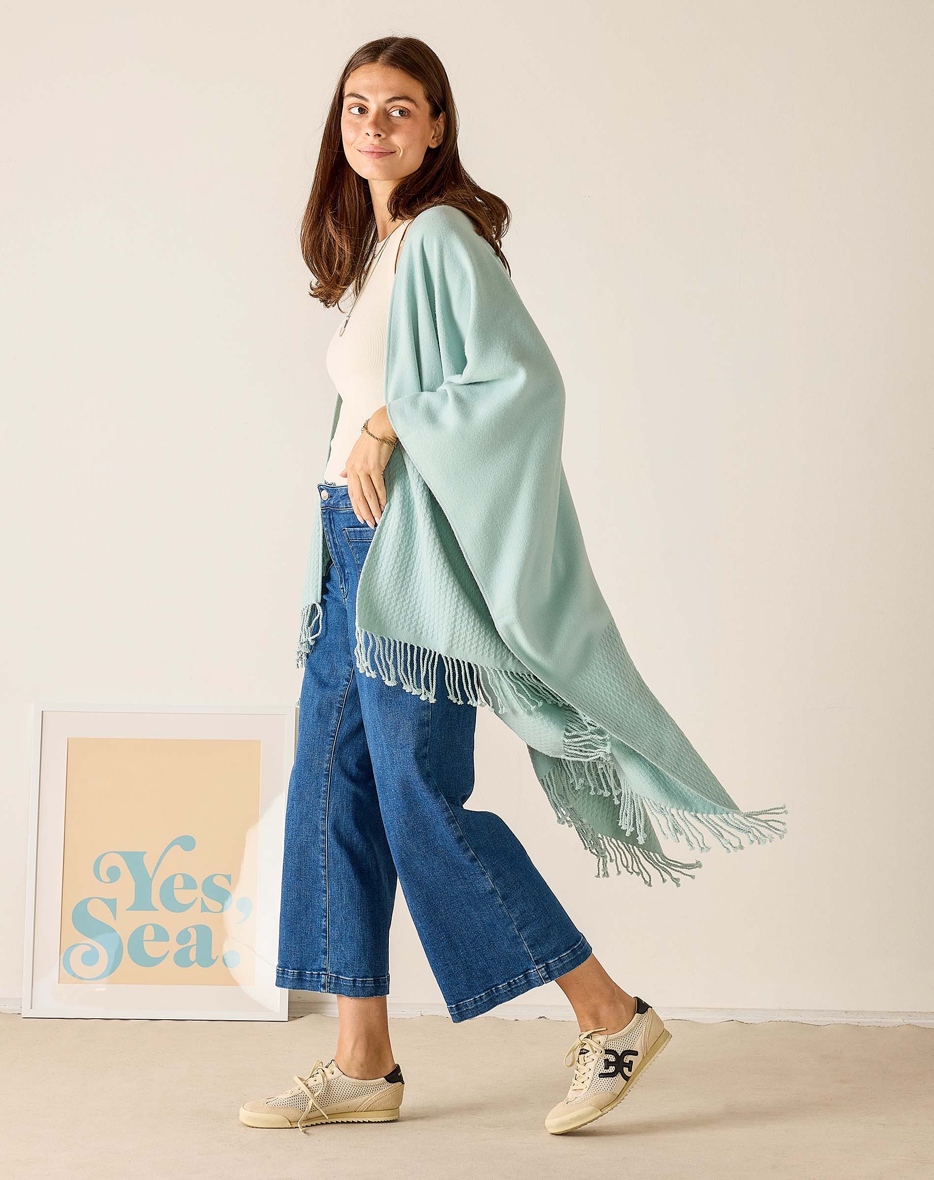 Woman wearing a light blue scarf with fringe, standing indoors against a plain background.