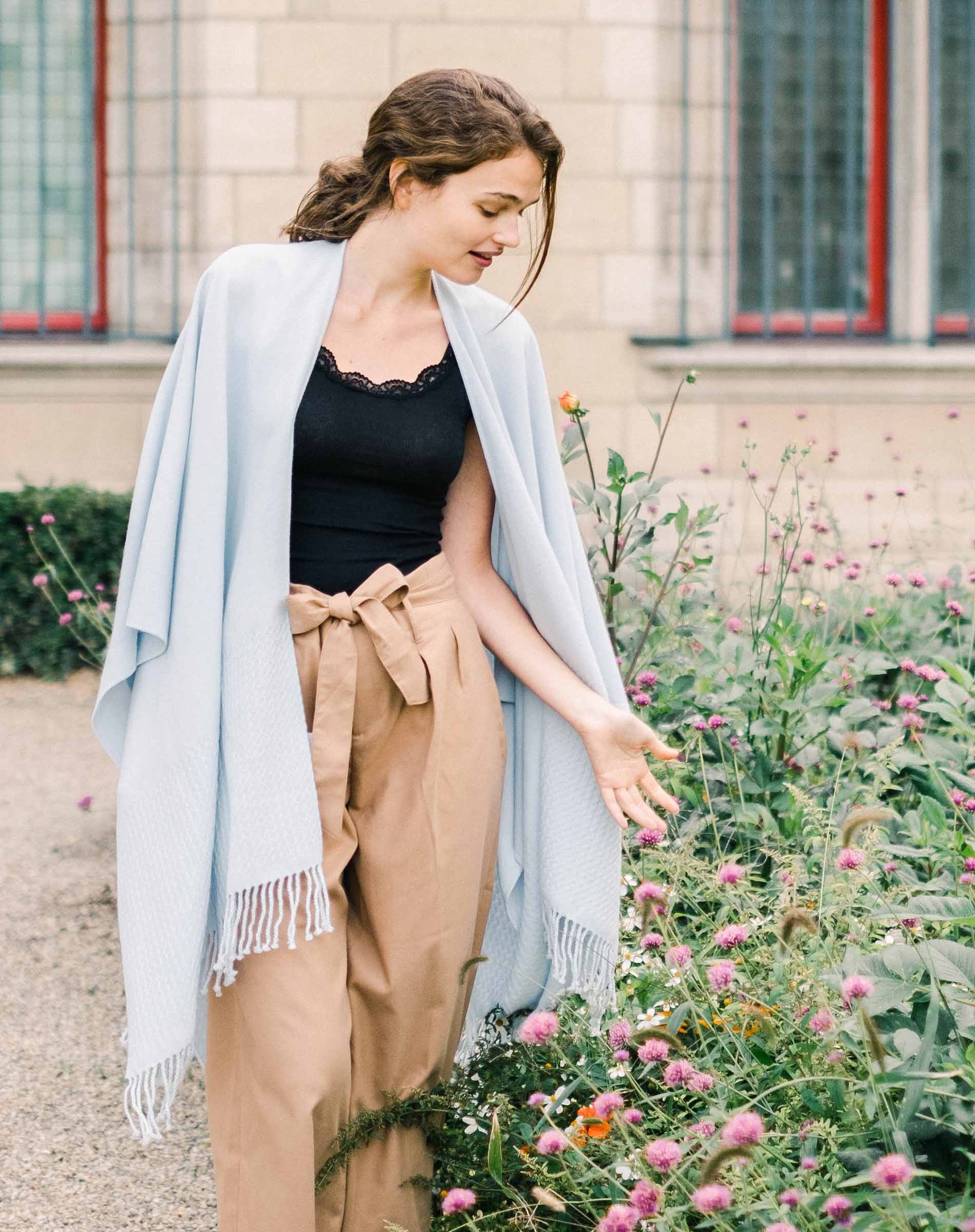 Woman standing in a garden with flowers and a building in the background