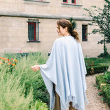 Woman wearing a light blue poncho in a garden setting with a building in the background