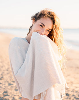 Curled hair female in a white wrap smiling on the beach