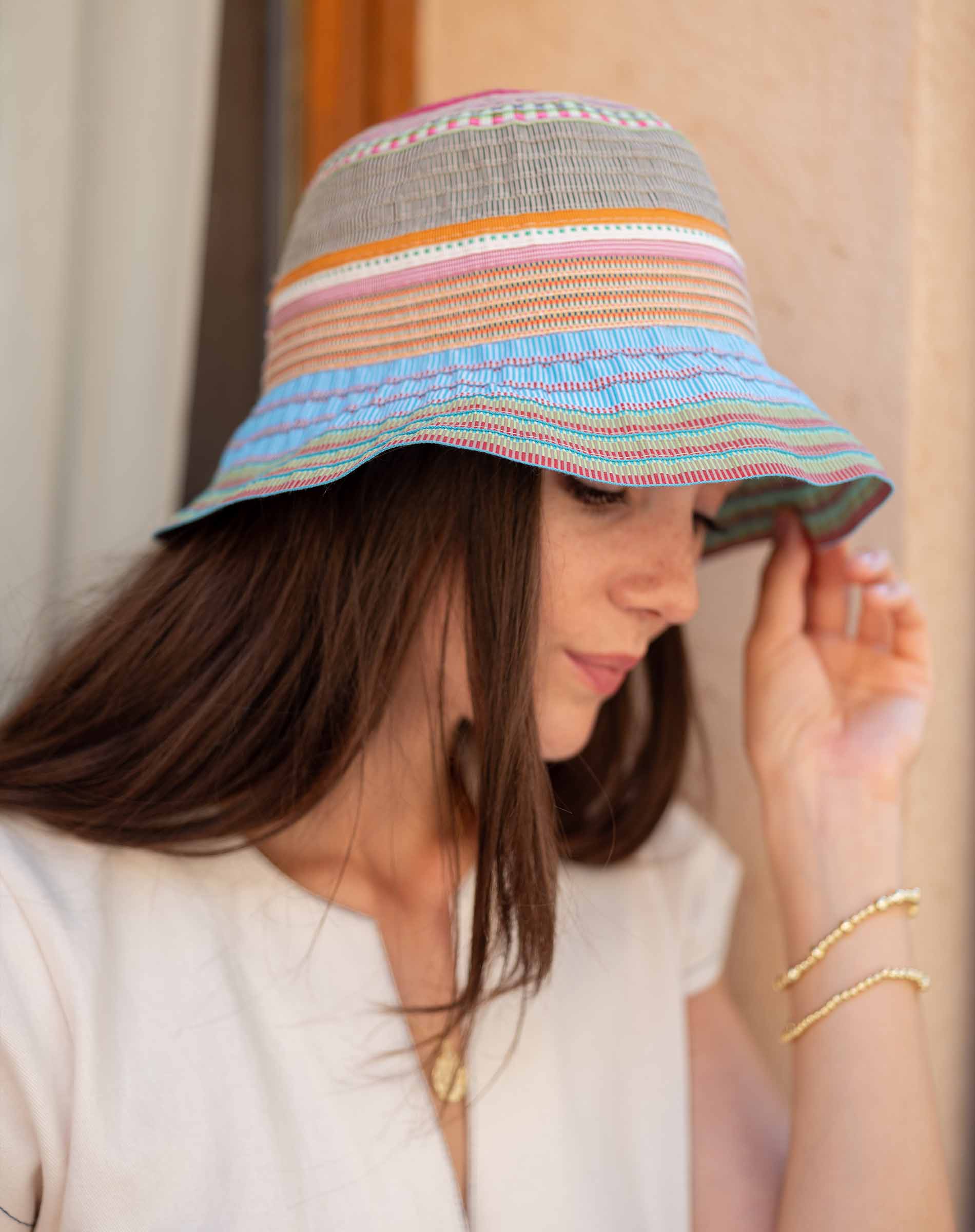 Woman wearing a colorful striped bucket hat against a neutral background