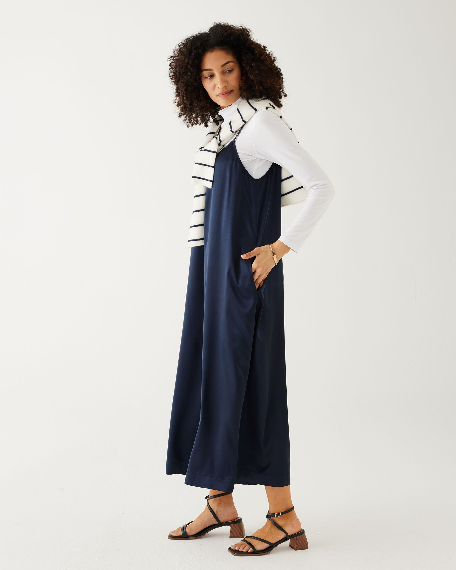 profile of woman wearing mersea coco satin jumpsuit in dark sapphire against white backdrop