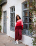 woman wearing mersea coco satin jumpsuit in garnet standing in front of building