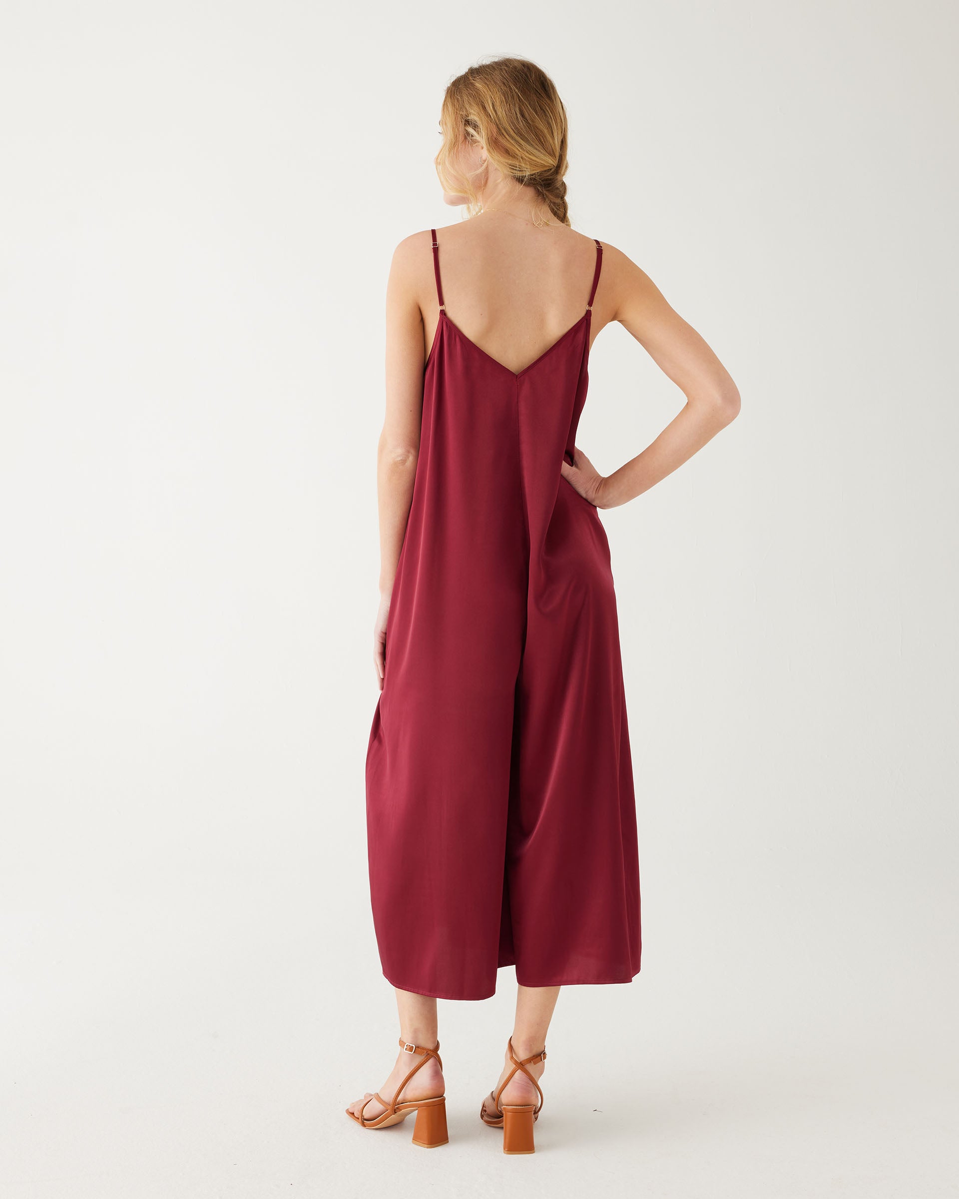 rearview of woman wearing mersea coco satin jumpsuit in garnet against white backdrop