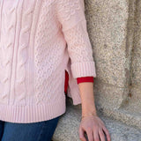 Petal pink cable knit sweater with ribbed trim and intricate stitch details.