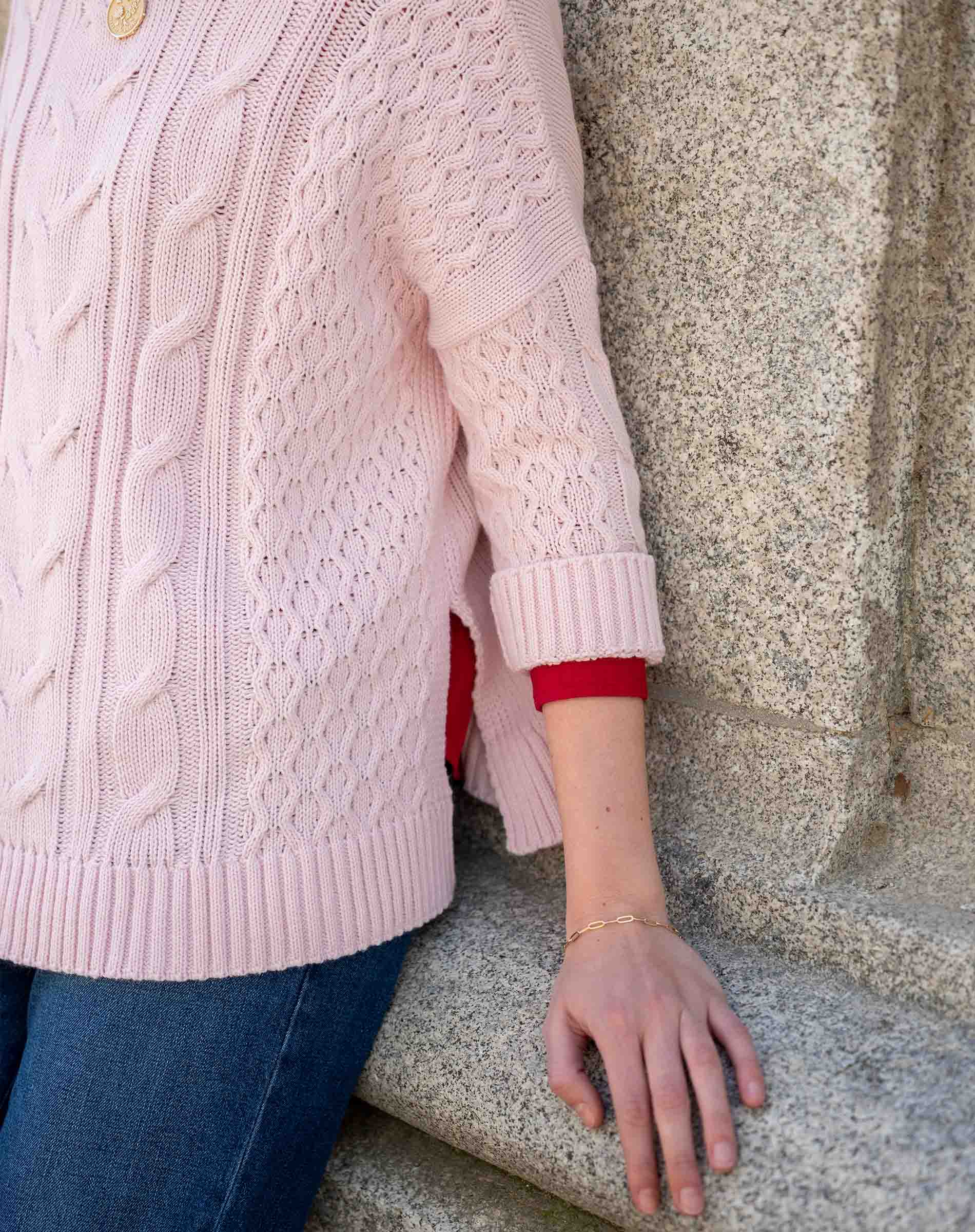 Petal pink cable knit sweater with ribbed trim and intricate stitch details.