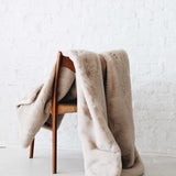 Mersea Cozy Cabin Faux Fur Throw Blanket in oatmeal draped over a chair