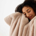 woman holding Mersea Cozy Cabin Faux Fur Throw Blanket in oatmeal up to her face