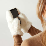 closeup of woman wearing mersea cozy cabin faux fur mittens in whisper white with exposed thumbs using phone