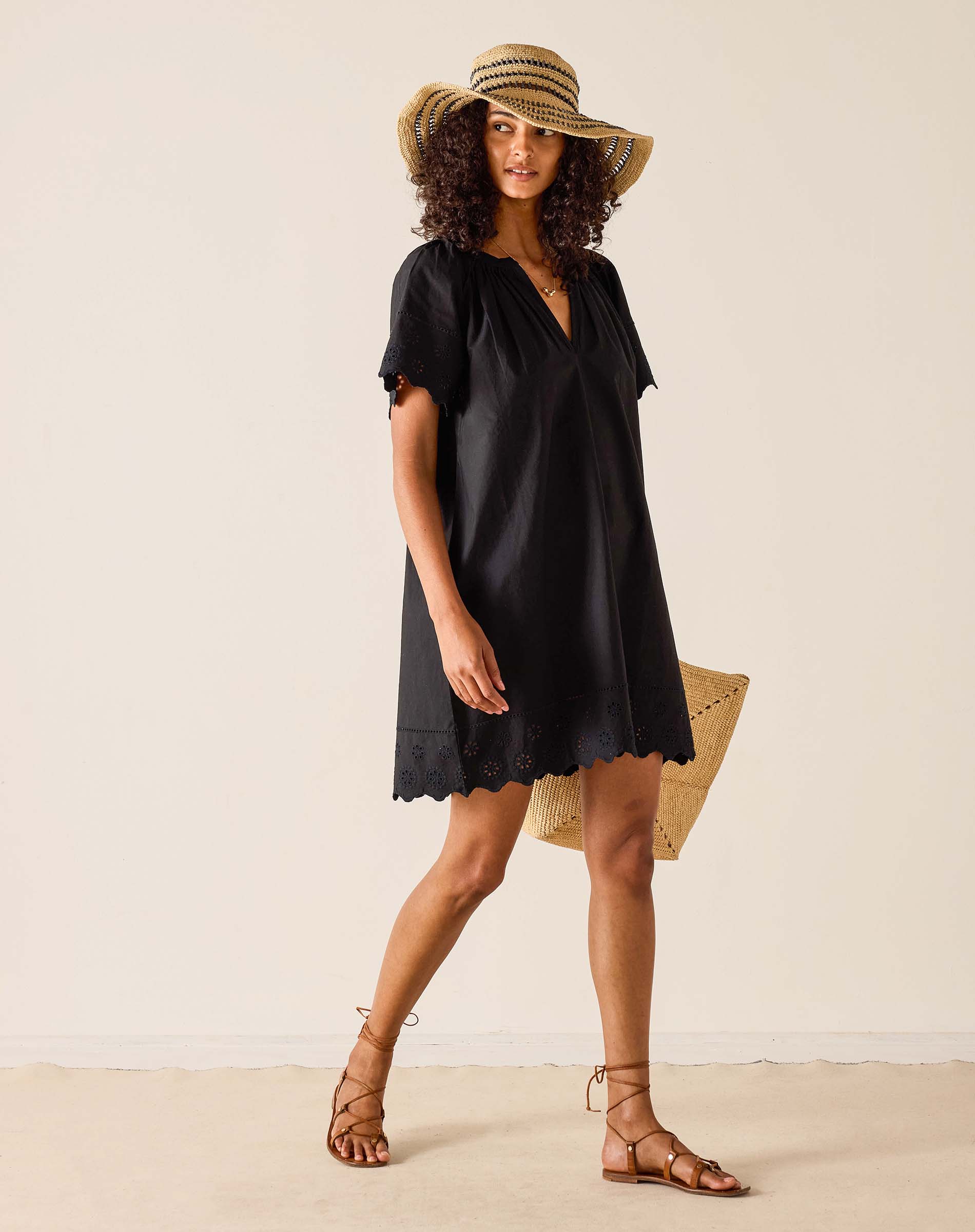 Woman wearing a black dress and straw hat on a plain background