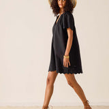 Woman wearing a black dress and straw hat against a plain background