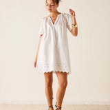 Woman wearing a white dress with lace details against a plain background