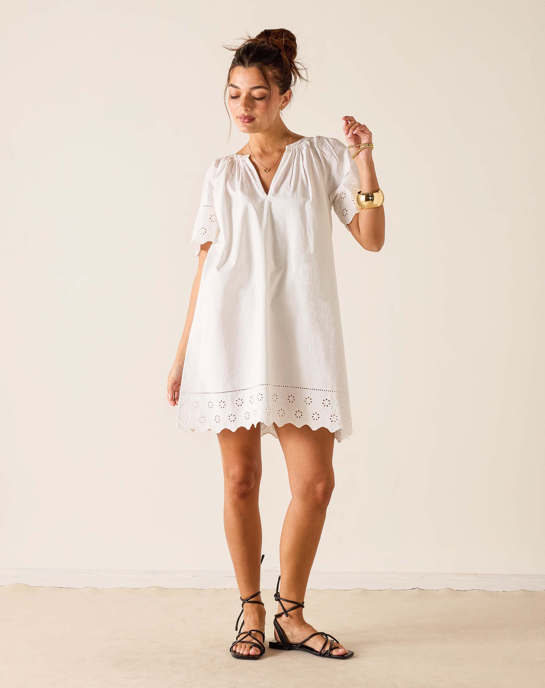 Woman wearing a white dress with lace details against a plain background