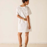 Woman wearing a white dress with lace details on a plain background