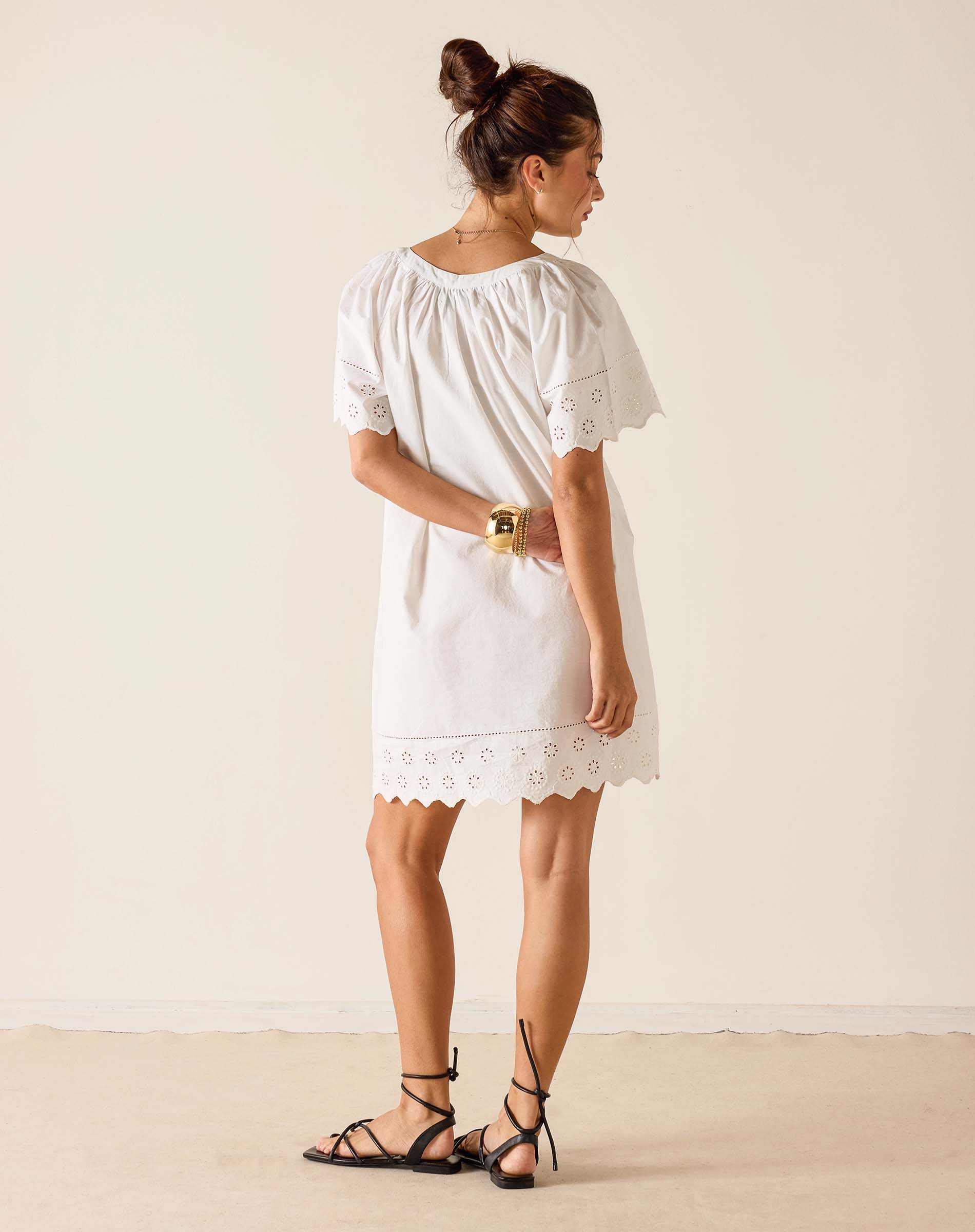 Woman wearing a white dress with lace details on a plain background
