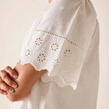 White dress with intricate cut-out patterns on sleeves against a neutral background